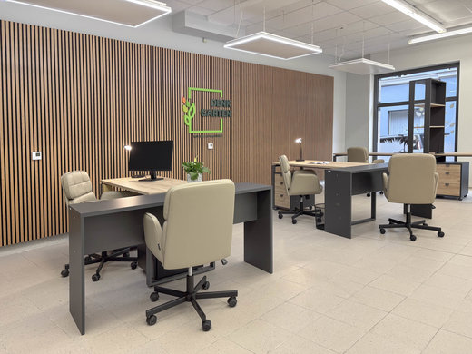 Mehrere Eckschreibtische stehen in einem Raum. Dazu stehen mehrere Schreibtischstühle an den Tischen. An der Wand hängt das DENKGARTEN Logo