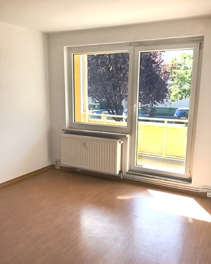 Auf dem Bild ist ein Zimmer mit einem Balkon zu sehen. Die Sonne scheint hinein.