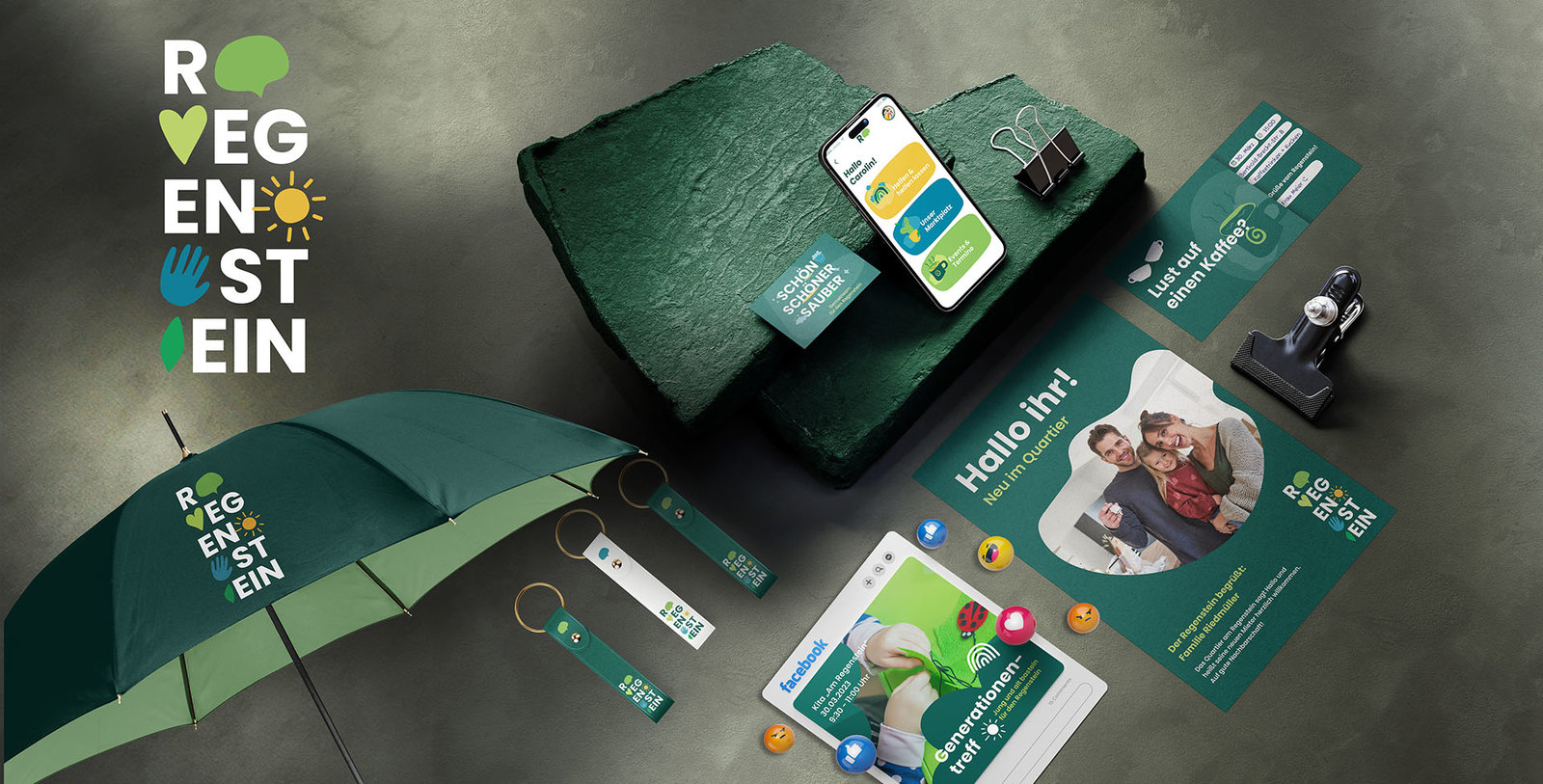Werbemittel des Quartiers Regenstein: Logo, Regenschirm, Schlüsselanhänger, Smartphone mit App, Flyer und Infomaterialien auf dunklem Untergrund.
