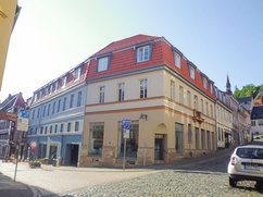 Eckgebäude an der Lange Straße 42 / Tränkestraße 21 in Blankenburg. Das sanierte Wohn- und Geschäftshaus mit heller Fassade und roten Dachgauben steht an einer gepflasterten Kreuzung in der historischen Altstadt.