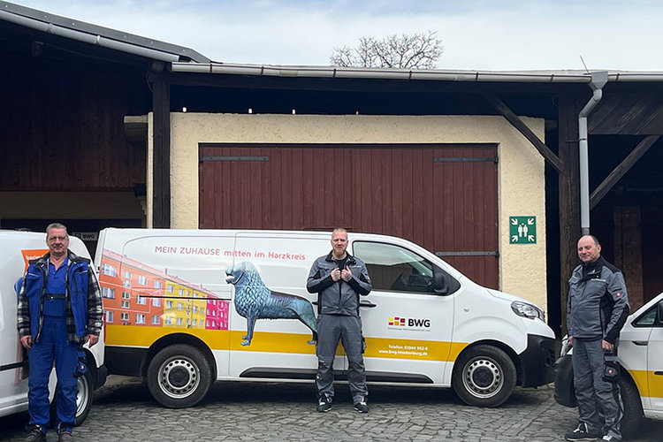 Drei Handwerker stehen vor einem Servicefahrzeug der BWG mit auffälliger Werbegrafik – Einsatzbereit für Hausmeisterdienste im Harzkreis