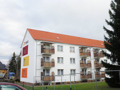 Rückseite der Wohnhäuser Halberstädter Straße 55 und 57 in Blankenburg mit frisch sanierter weißer Fassade, Balkonen mit Holzverkleidung und farbigen Akzentflächen in Rot, Gelb und orange an der Giebelseite. 