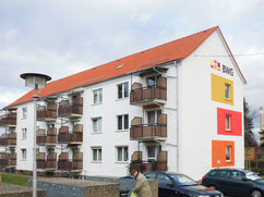 Rückansicht der sanierten Wohnhäuser Halberstädter Straße 55 und 57 in Blankenburg. Das Gebäude hat weiße Fassaden mit farbigen Elementen in Gelb, Orange und Rot sowie Balkone mit Holzverkleidung. Auf der Giebelseite ist das BWG-Logo gut sichtbar. 