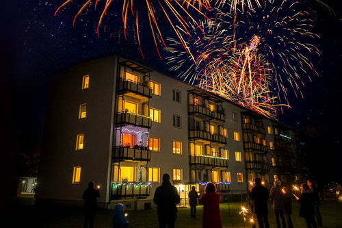 Das Bild zeigt ein BWG Gebäude. Davor stehen Menschen, welche das Feuerwerk hinter dem Gebäude betrachten.