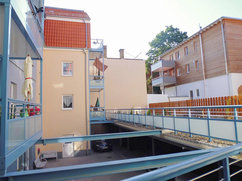 Innenhofansicht des Gebäudekomplexes Lange Straße 42 / Tränkestraße 21 in Blankenburg. Sicht auf Balkone, einen überdachten Stellplatzbereich und moderne Verbindungsstege mit Glas- und Metallgeländern. 