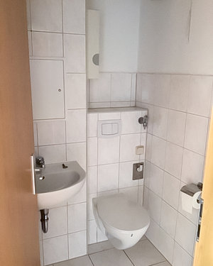 Das Bild zeigt ein Badezimmer mit weißen Fliesen. Zu sehen ist eine Toilette und ein Waschbecken.
