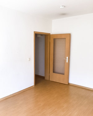 Das Bild zeigt einen Raum mit einer geöffneten braunen Tür. Die Tür hat eine Glasscheibe in der Mitte.