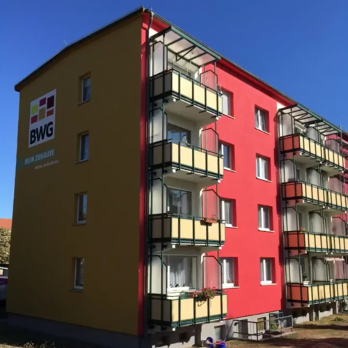Frisch sanierte Fassade eines Mehrfamilienhauses in der Karl-Zerbst-Straße in Blankenburg mit BWG-Logo und Balkonen in den Unternehmensfarben Gelb und Rot.