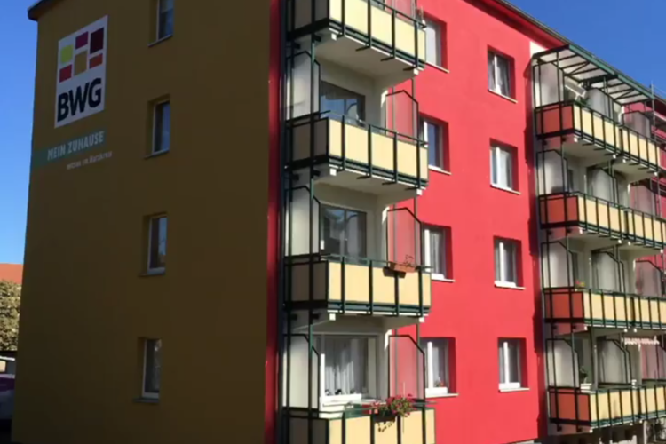 Frisch sanierte Fassade eines Mehrfamilienhauses in der Karl-Zerbst-Straße in Blankenburg mit BWG-Logo und Balkonen in den Unternehmensfarben Gelb und Rot.