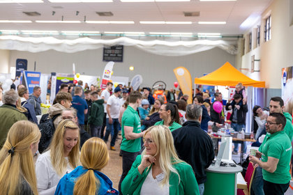 Blick in eine gut besuchte Messehalle mit zahlreichen Ausstellern und Besuchergruppen, bunte Messestände, Infomaterialien und Gespräche prägen das lebendige Veranstaltungsgeschehen
