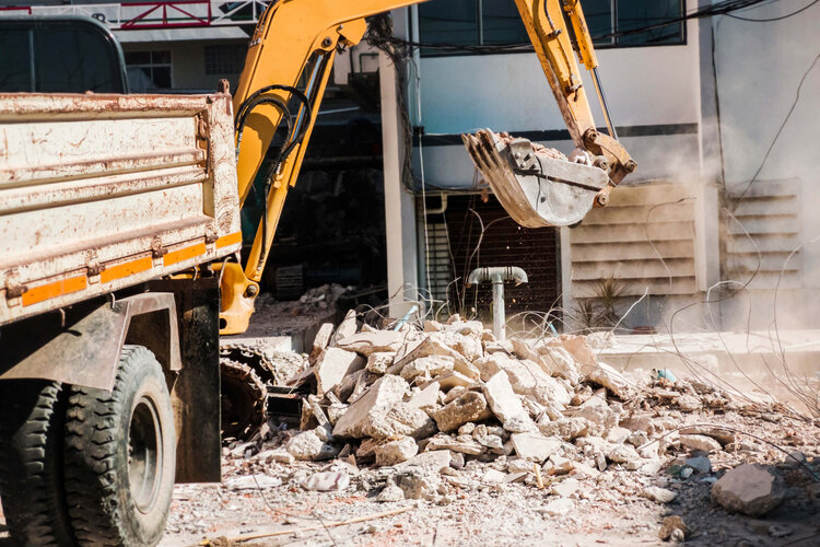 Abrissarbeiten mit Bagger und Lkw – Baumaschinen räumen Bauschutt vor Wohngebäude