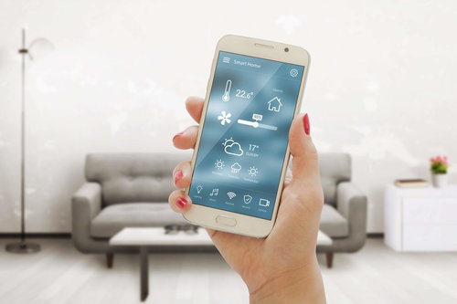 Smartphone mit Smart-Home-App zur Steuerung von Temperatur, Licht und Sicherheit – moderne Wohntechnologie im Wohnzimmer mit grauem Sofa im Hintergrund