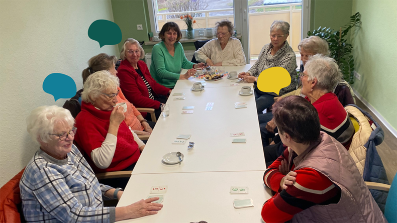 Eine Gruppe älterer Menschen sitzt gemeinsam an einem langen Tisch, spielen Karten und unterhalten sich.