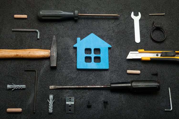 Symbolisches Haus mit Handwerkzeugen auf schwarzem Untergrund – Renovierung und Heimwerken.