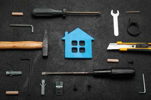 Symbolisches Haus mit Handwerkzeugen auf schwarzem Untergrund – Renovierung und Heimwerken.