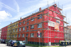 Frontansicht der Wohnhäuser Börnecker Straße 36–38 im Quartier Regenstein während der farblichen Fassadensanierung. Die Gebäude sind eingerüstet und leuchten in kräftigen Rot- und Gelbtönen. Ein Bauschild weist auf die Sanierungsmaßnahme hin.