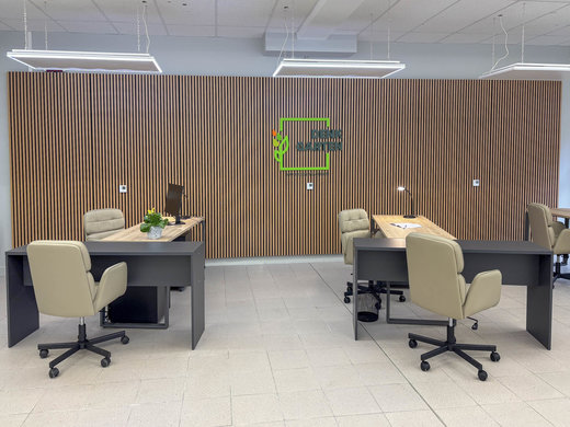 Mehrere Eckschreibtische stehen in einem Raum. Dazu stehen mehrere Schreibtischstühle an den Tischen. An der Wand hängt das DENKGARTEN Logo