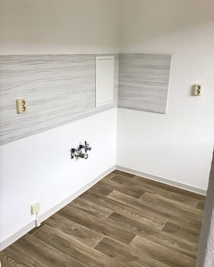 Auf dem Bild wird die Küche ohne Möbilierung gezeigt. An der wand befinden Platten zum Schutz der Wand.