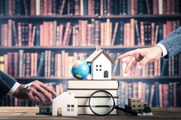 Büchern, Lupe, Globus und Miniaturhäusern vor Bücherregal – Mieter und Gesetze