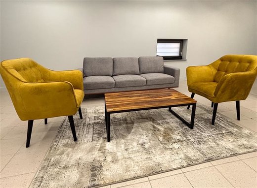 Zwei gelber Sessel stehen an einem Tisch, sowie ein graues Sofa. Die Möbel stehen auf einem grauen Teppich