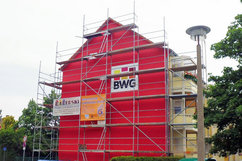 Giebelseite der Wohnhäuser Börnecker Straße 36–38 im Quartier Regenstein mit vollständig eingerüsteter, leuchtend roter Fassade. An der Fassade sind Werbebanner des Bauunternehmens und der Wohnungsbaugesellschaft BWG angebracht.