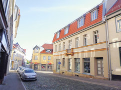 Straßenszene an der Ecke Lange Straße 42 / Tränkestraße 21 in Blankenburg. Zu sehen ist ein saniertes Wohn- und Geschäftsgebäude mit heller Fassade und roten Dachgauben.