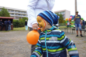 Kind mit Luftballon und Tiger-Gesicht bemalt beim Fest im Wohngebiet.