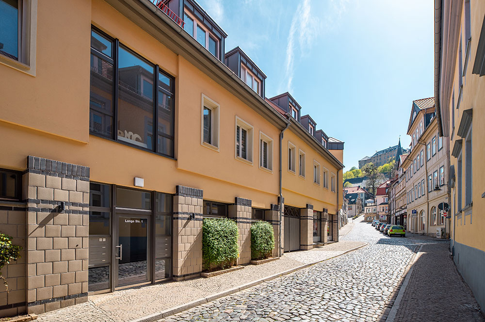 Moderne Wohn- und Geschäftshausfassade in der Lange Straße 1 in Blankenburg (Harz) mit Kopfsteinpflaster und Blick auf das Schloss.